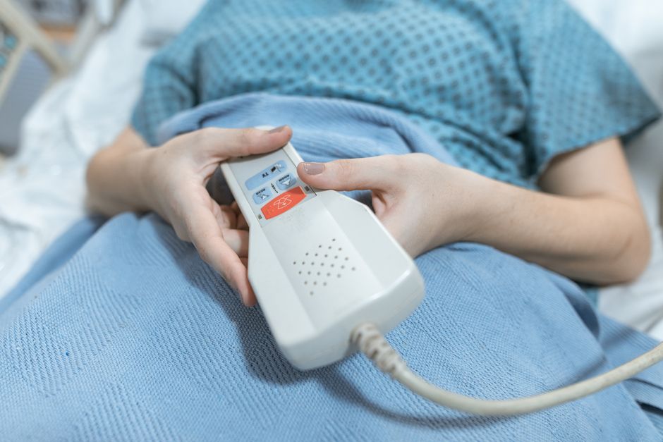 Pacjent sięga po przycisk przywoławczy przy łóżku szpitalnym.