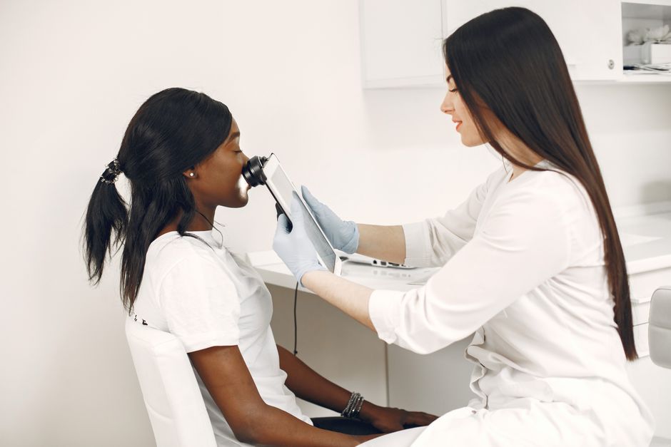 Gabinet dermatologiczny: lekarz w fartuchu przy biurku obok leżanki, na tacy leży dermatoskop, a na krześle złożona koszula.
