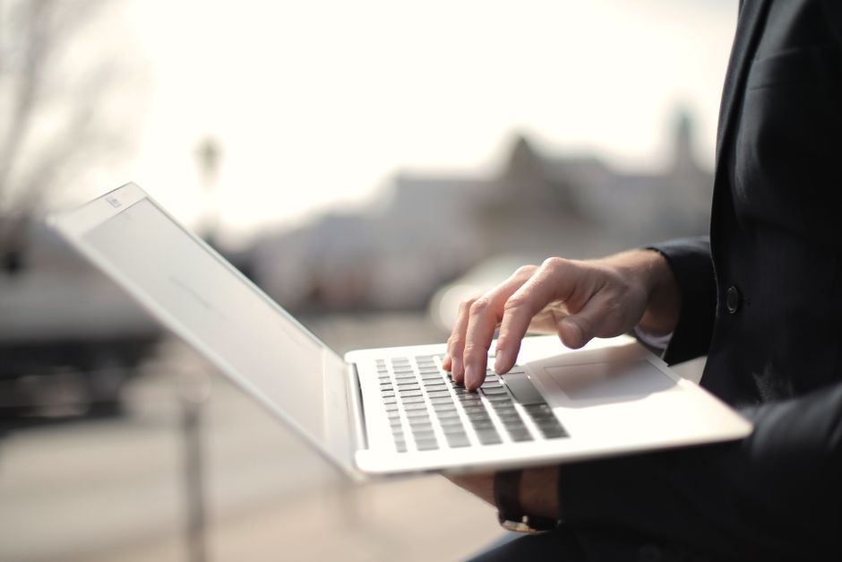 Osoba przy kuchennym stole z laptopem i telefonem sprawdza w internecie dostępne terminy wizyt i badań.