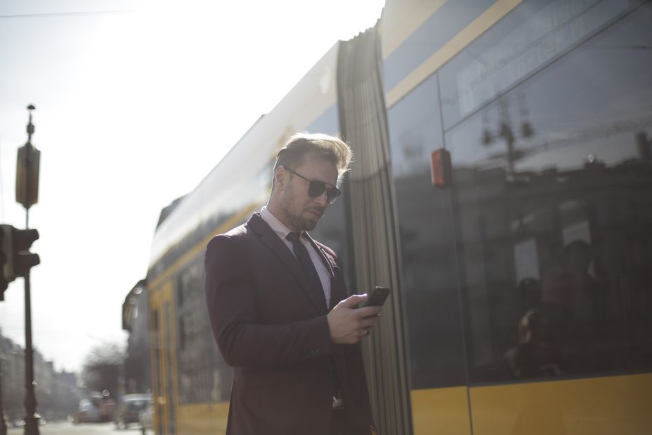 Mężczyzna stoi na miejskim chodniku i sprawdza termin na smartfonie, trzymając w ręku złożoną kartkę.