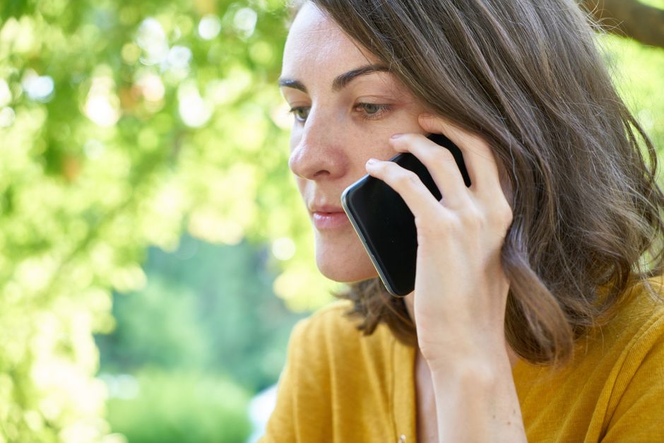 Mężczyzna rozmawia przez telefon na ławce w parku, w tle zielony park i ścieżka w słoneczny dzień.
