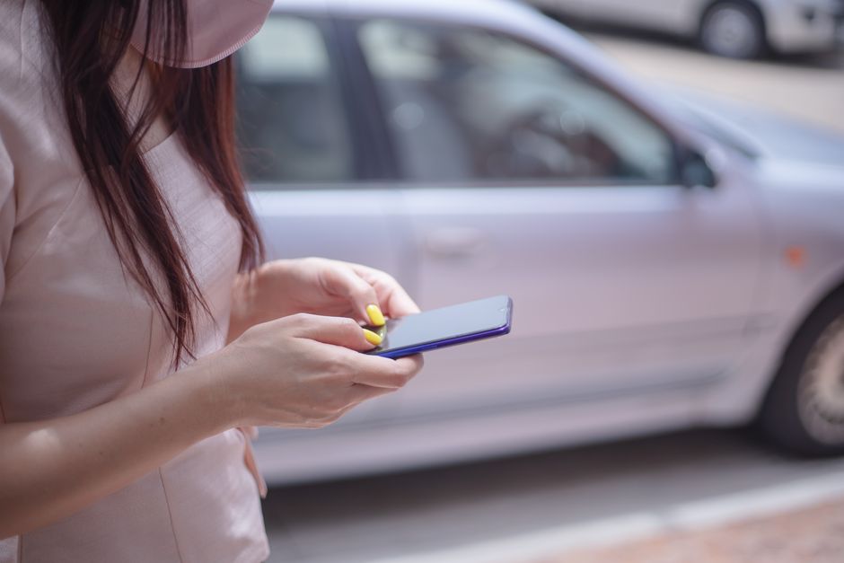 Osoba siedzi na ławce w parku i przegląda na smartfonie listę poradni, obok leży otwarty notes.