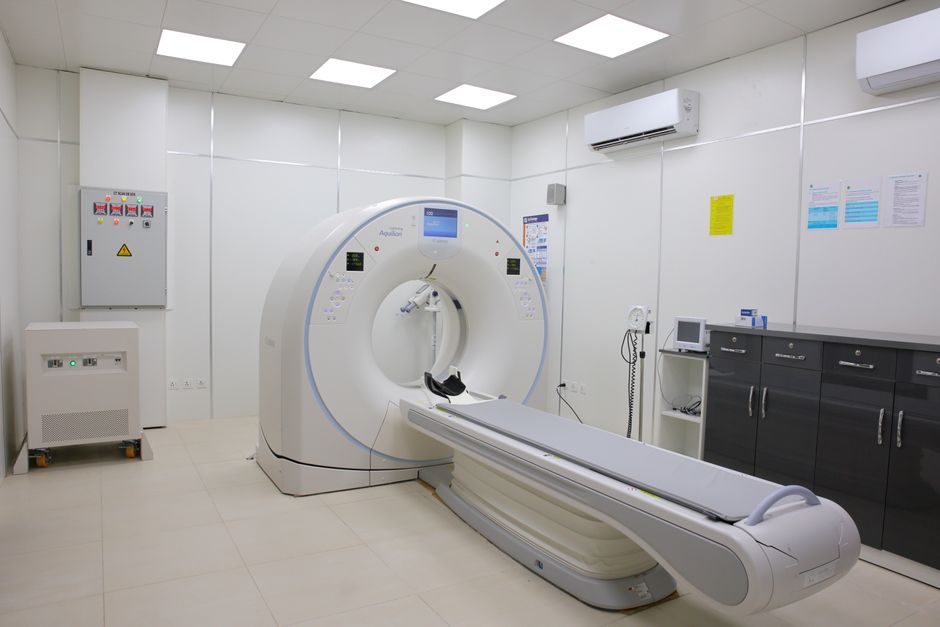 Pacjent leżący na stole tomografu w jasnym gabinecie diagnostycznym, w tle monitor sterujący badaniem.