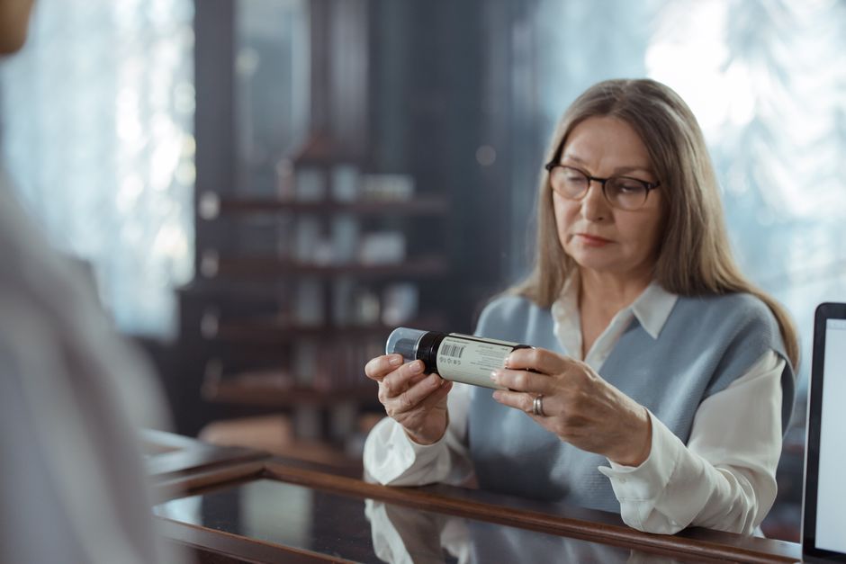 Osoba w domu sprawdza boczną ściankę pudełka z lekiem.