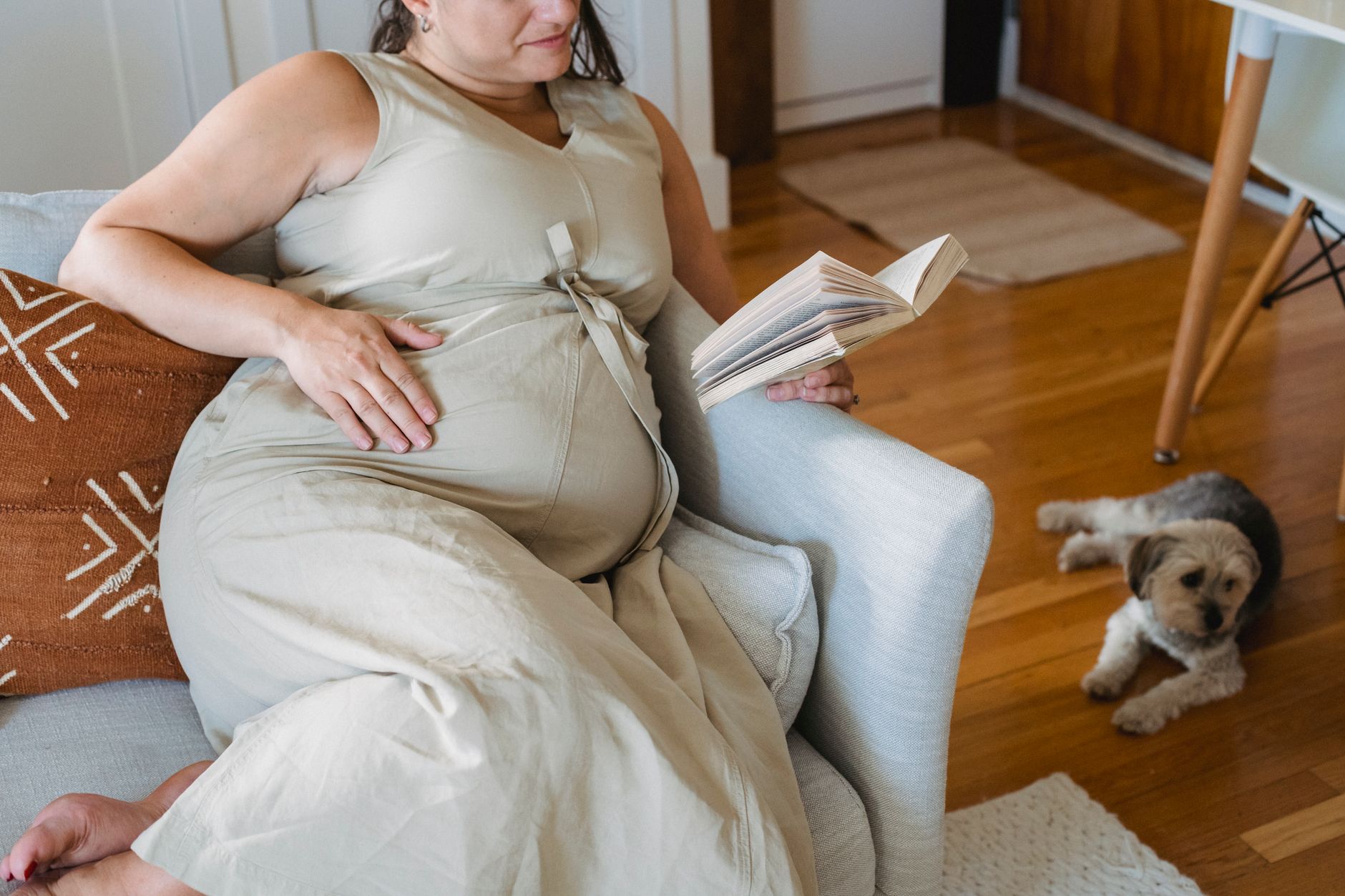 Pr pregnant woman siedzi na kanapie, trzymając się za brzuch w ciepłym świetle słonecznym.